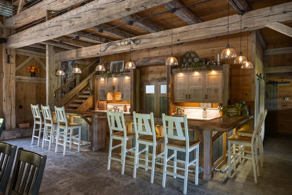 Bar area with exposed white oak beams, pendant lighting and sliding barn doors inside the Dover Party Barn