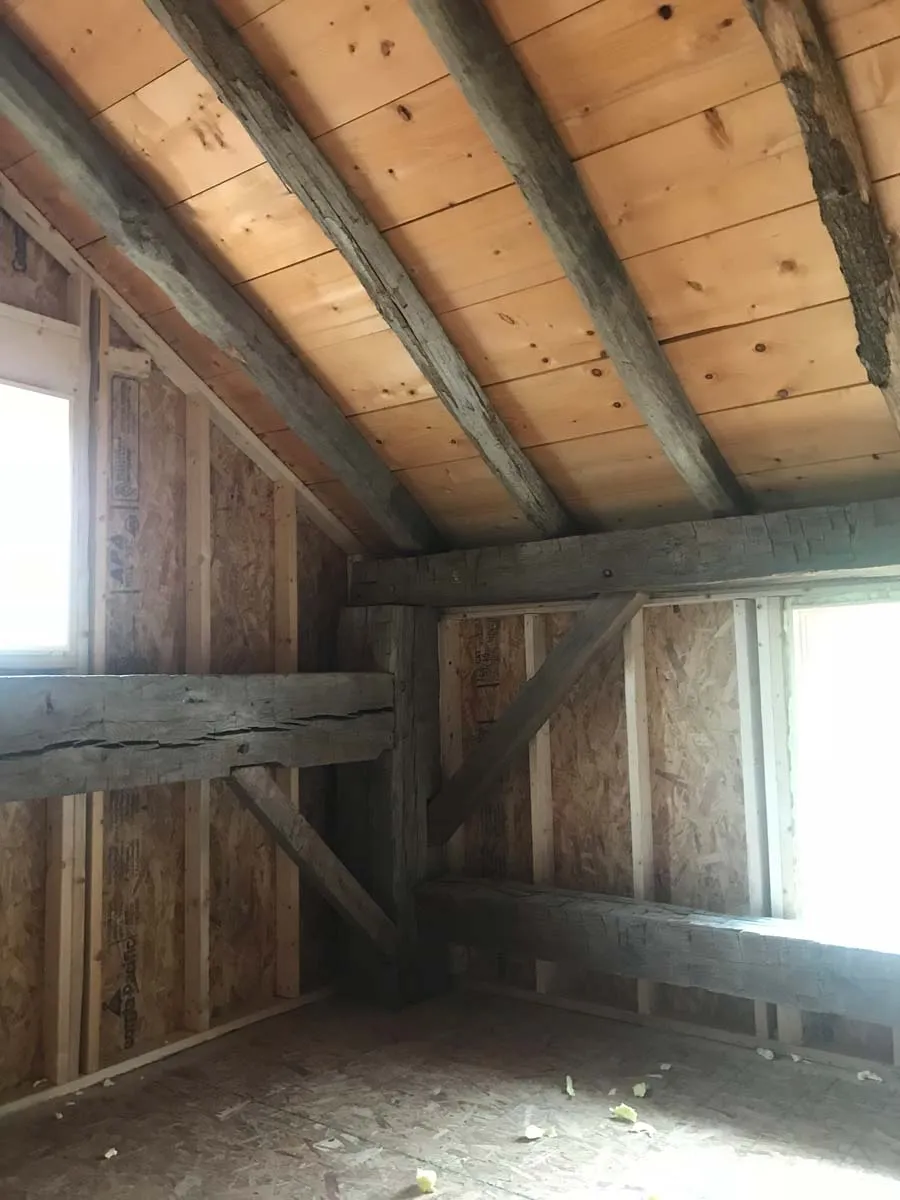 Hand-hewn beams framed by new insulated walls and windows inside a barn home loft