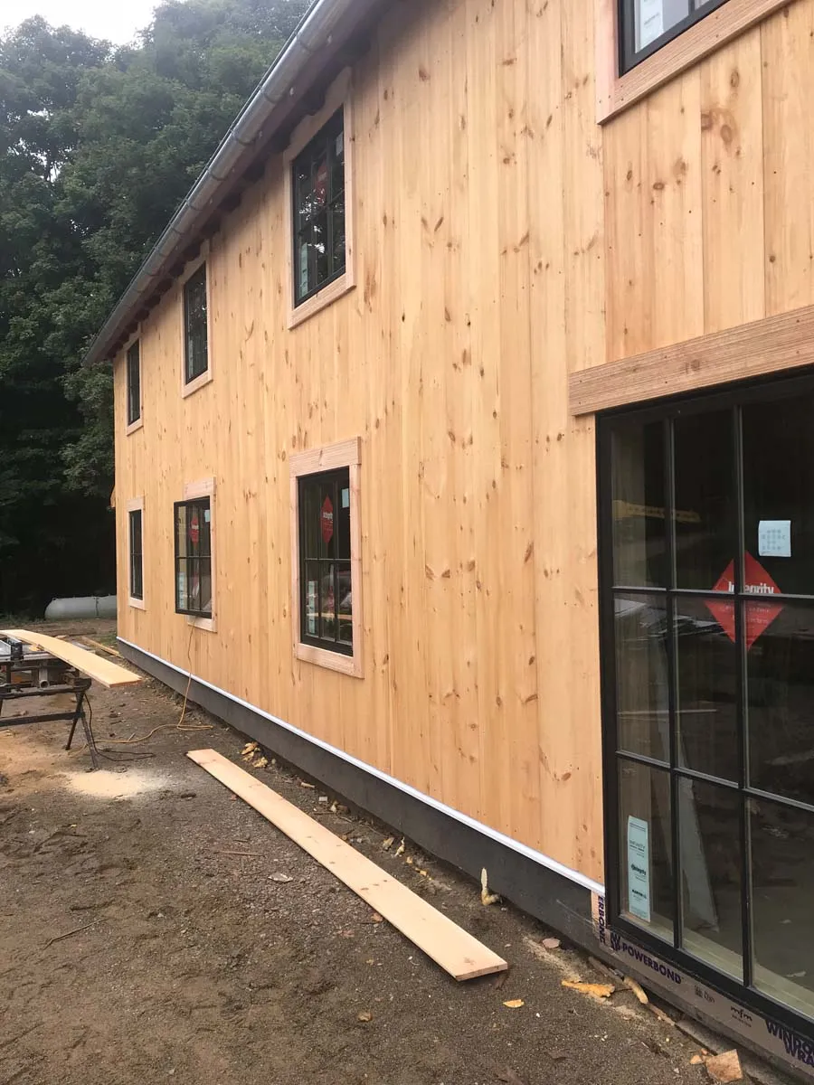 New vertical pine board siding and black-framed windows on a timber frame barn home exterior